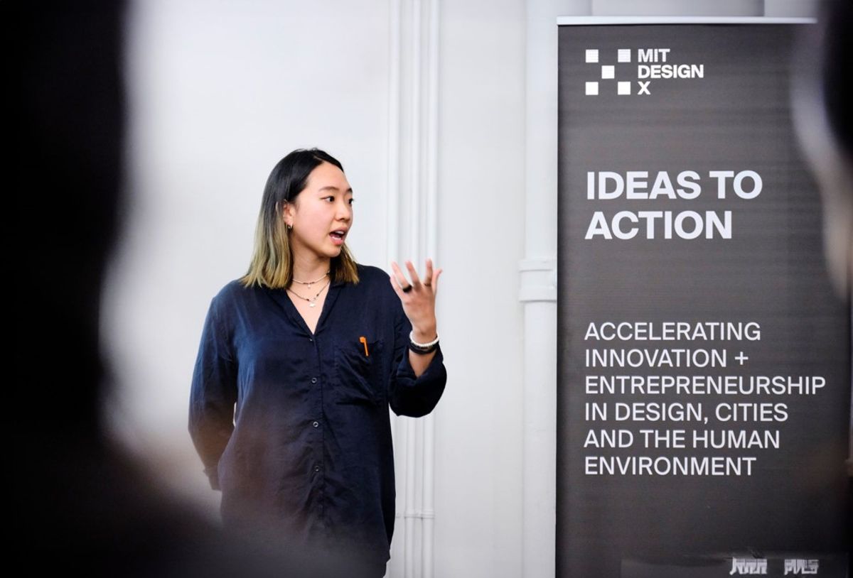 A person presents next to a banner that reads, "MIT DesignX, Ideas to Action."