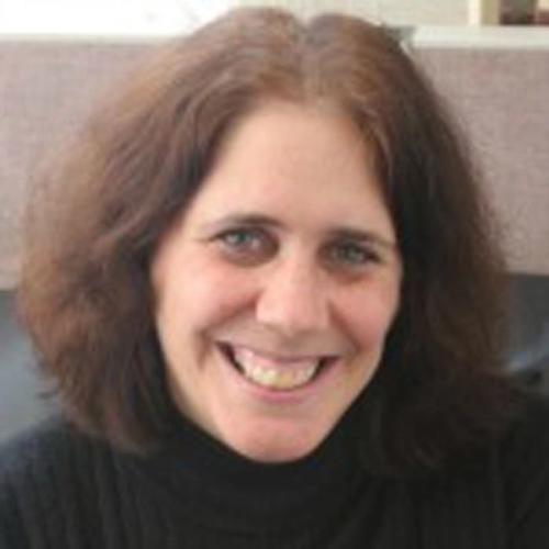 A woman with shoulder-length brown hair smiles at the camera. She is wearing a black turtleneck sweater, and the background appears to be an indoor setting.