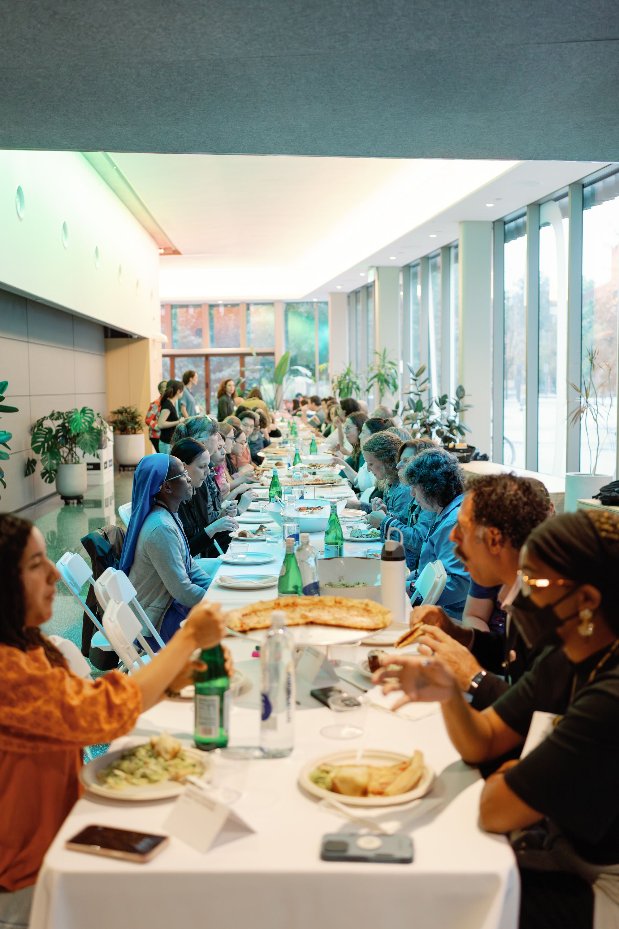 Participants share lunch in a long line of tables in the MIT Welcome Center.
