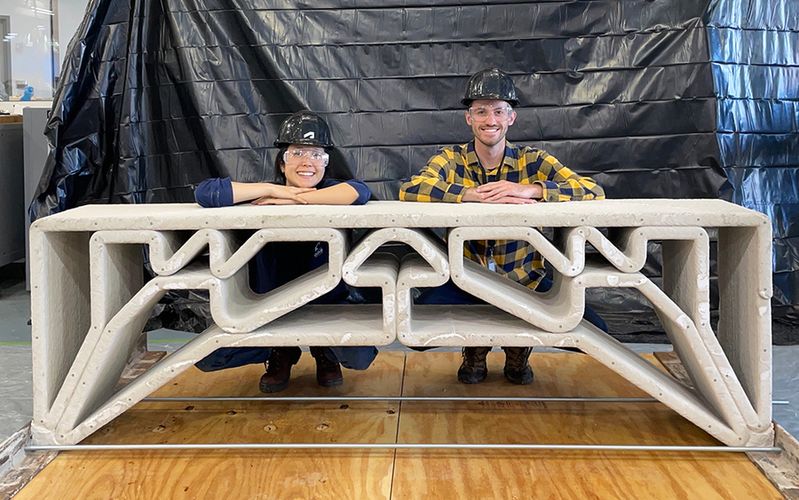 MIT Department of Civil and Environmental Engineering postdoc Hajin Kim-Tackowiak (left) and graduate student Zane Schemmer pose with the 3D-printed concrete bridge they designed and load-tested.