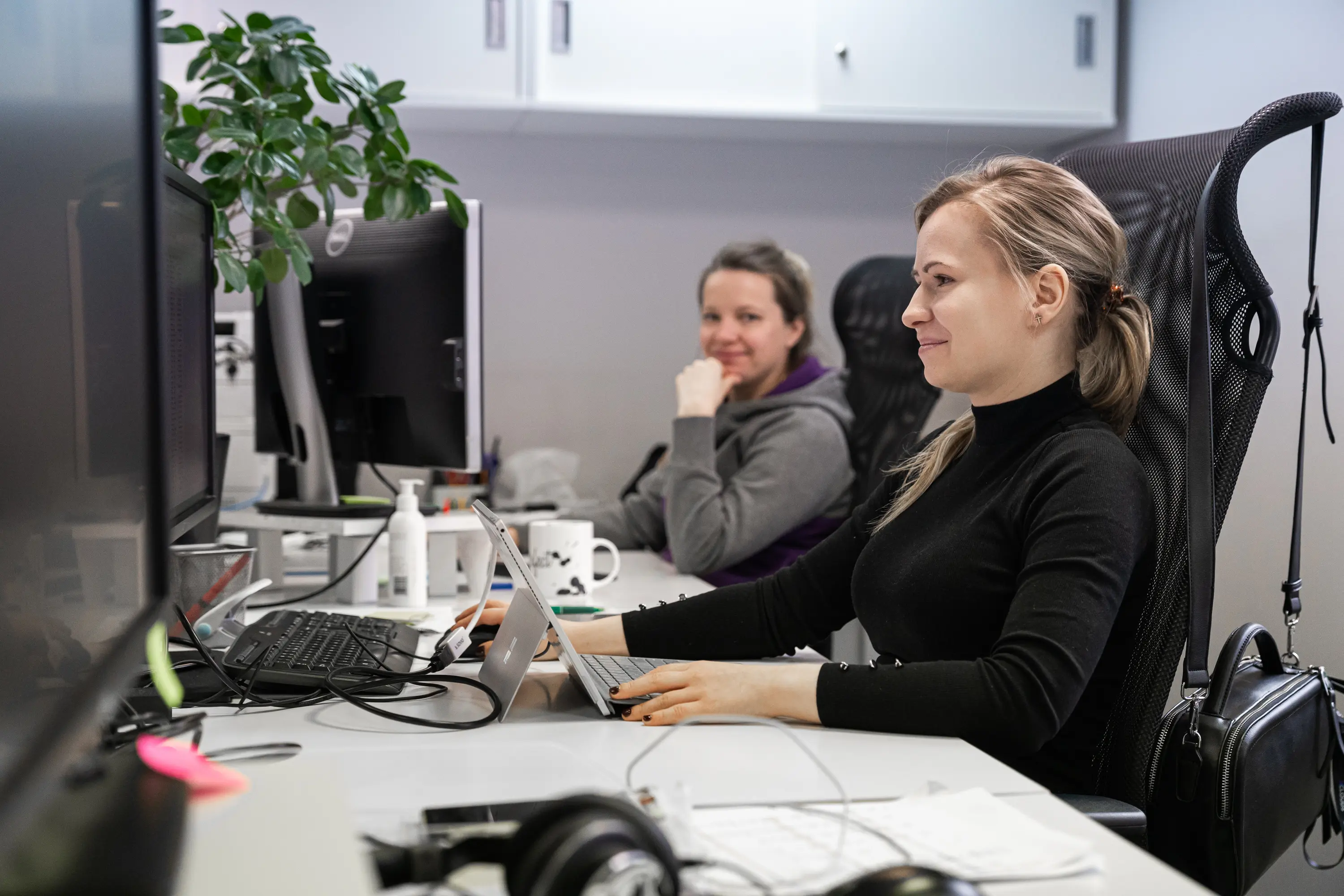 A girl with long hair sitting at an office desk coding. 