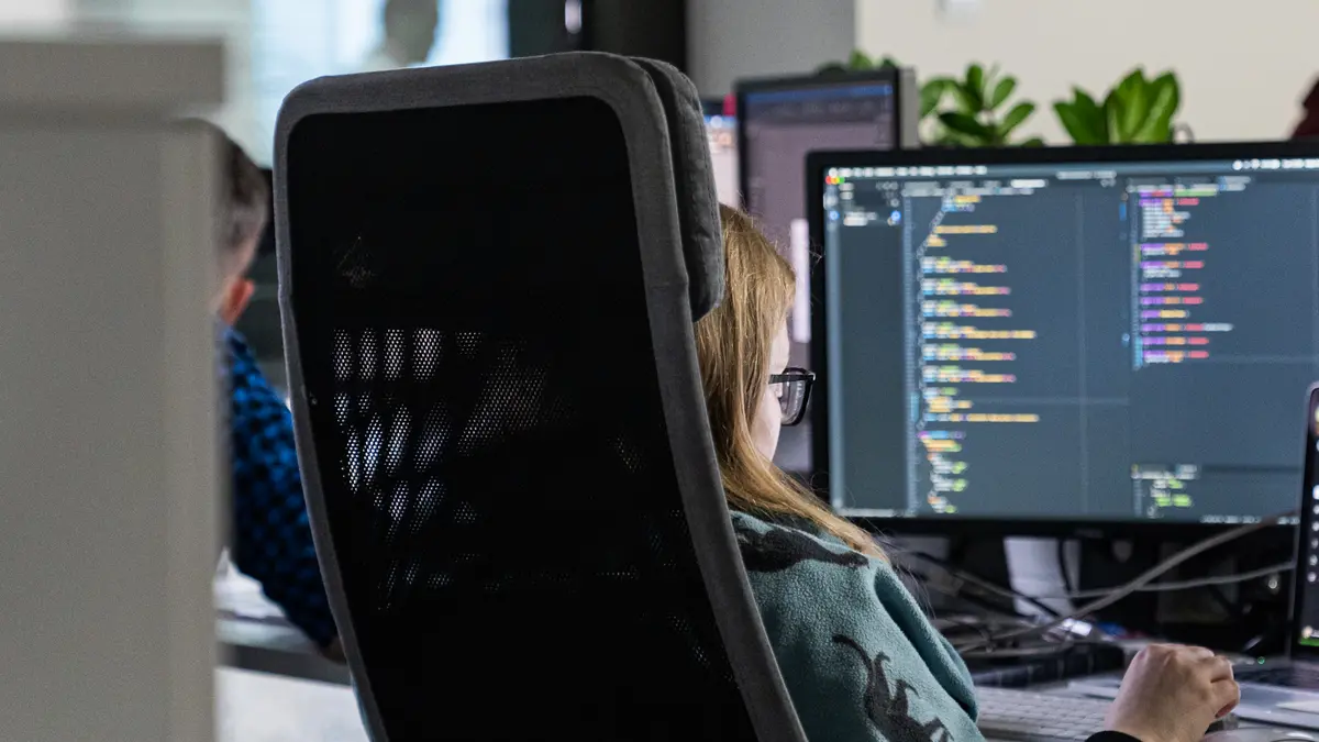 Woman working at a desk with code on a dark screen
