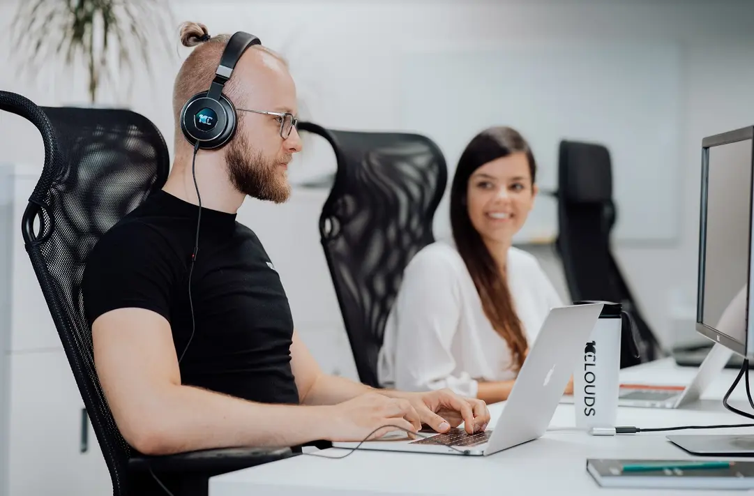 A man and woman working at their laptops on a white desk