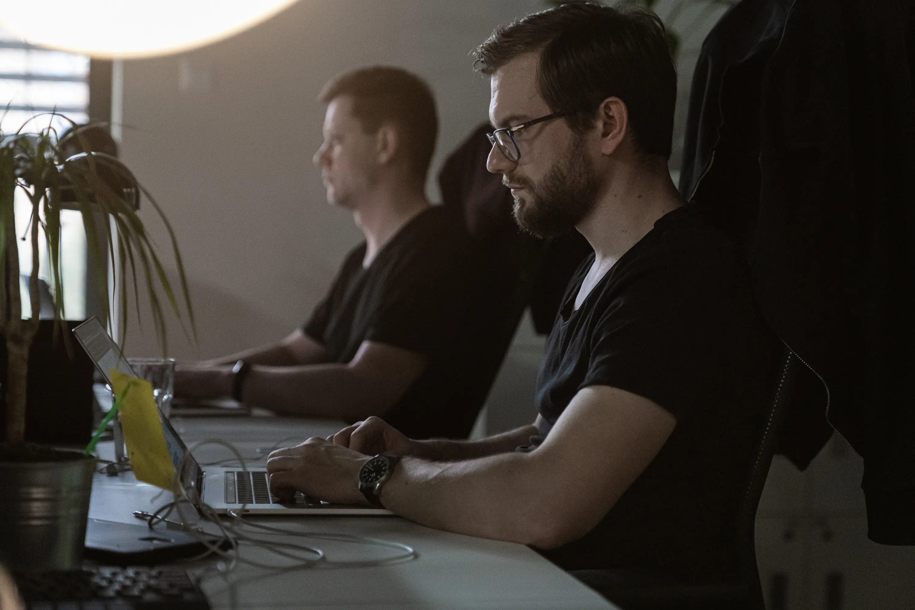 Two developers working on laptops at an office desk