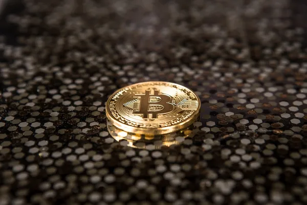 A single bitcoin on a brown and black speckled background