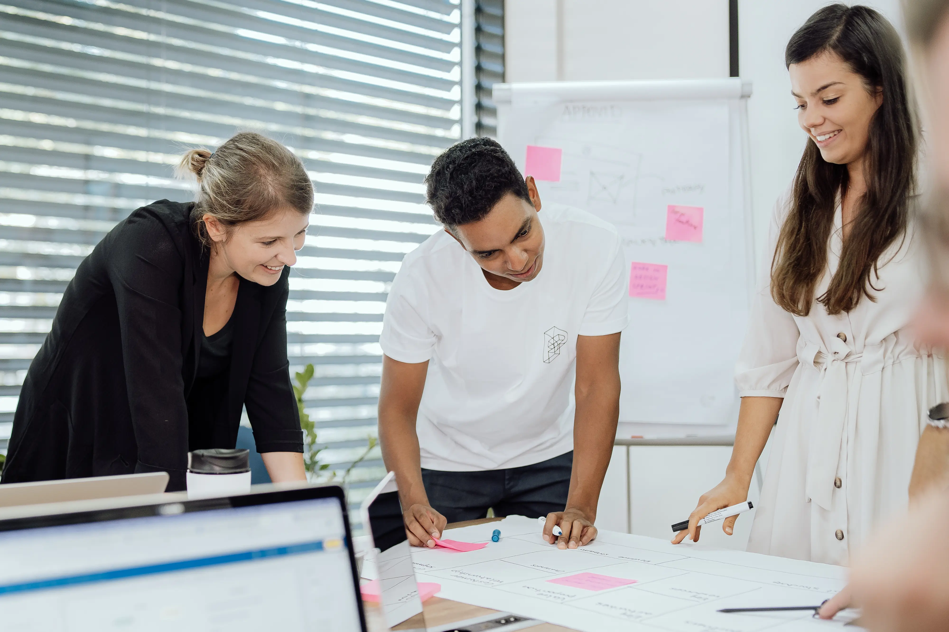 Two women and one man gathered around a desk in a boardroom looking at the results of a usability test on a large sheet of paper.