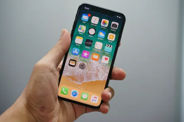 Image of a man's hand holding an Apple iPhone with the homescreen on show featuring all the apps