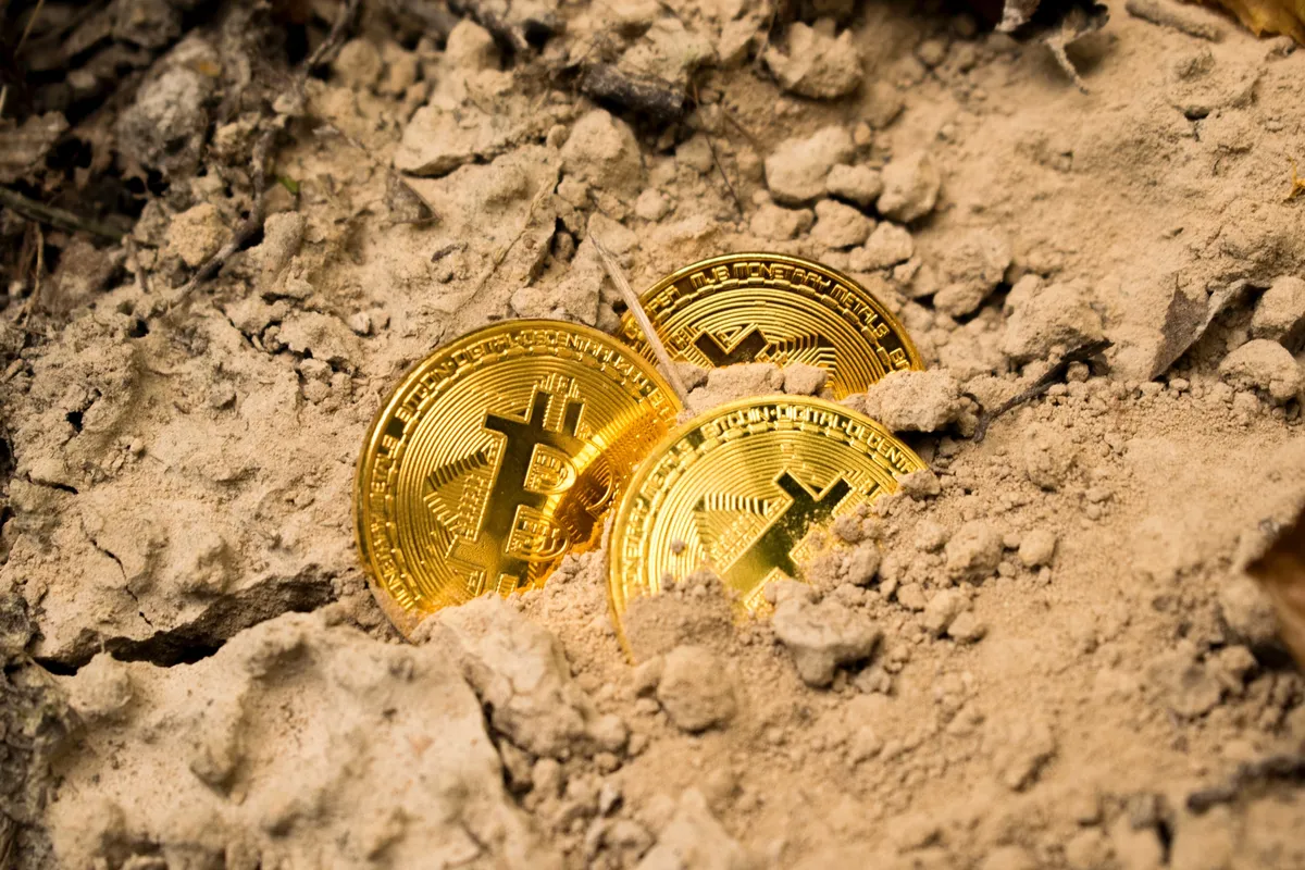Three Bitcoin coins buried in sand