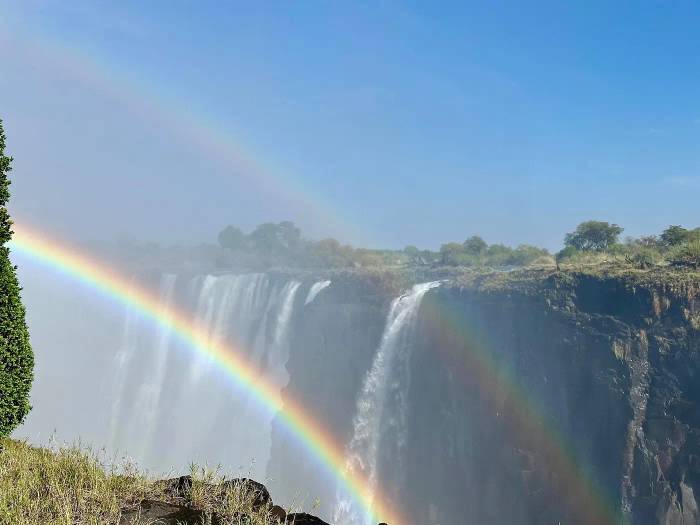 Our American guests from Florida capturing a rainbow arching over Victoria Falls, observing hippos in the Zambezi River, and viewing their outside suite at Victoria Falls River Lodge - Island Treehouse Suites