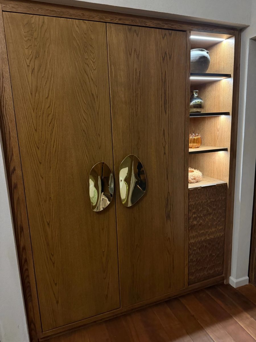 Oak wardrobe with sculpted polished brass handles and lit display shelves in a Kuganha tented suite