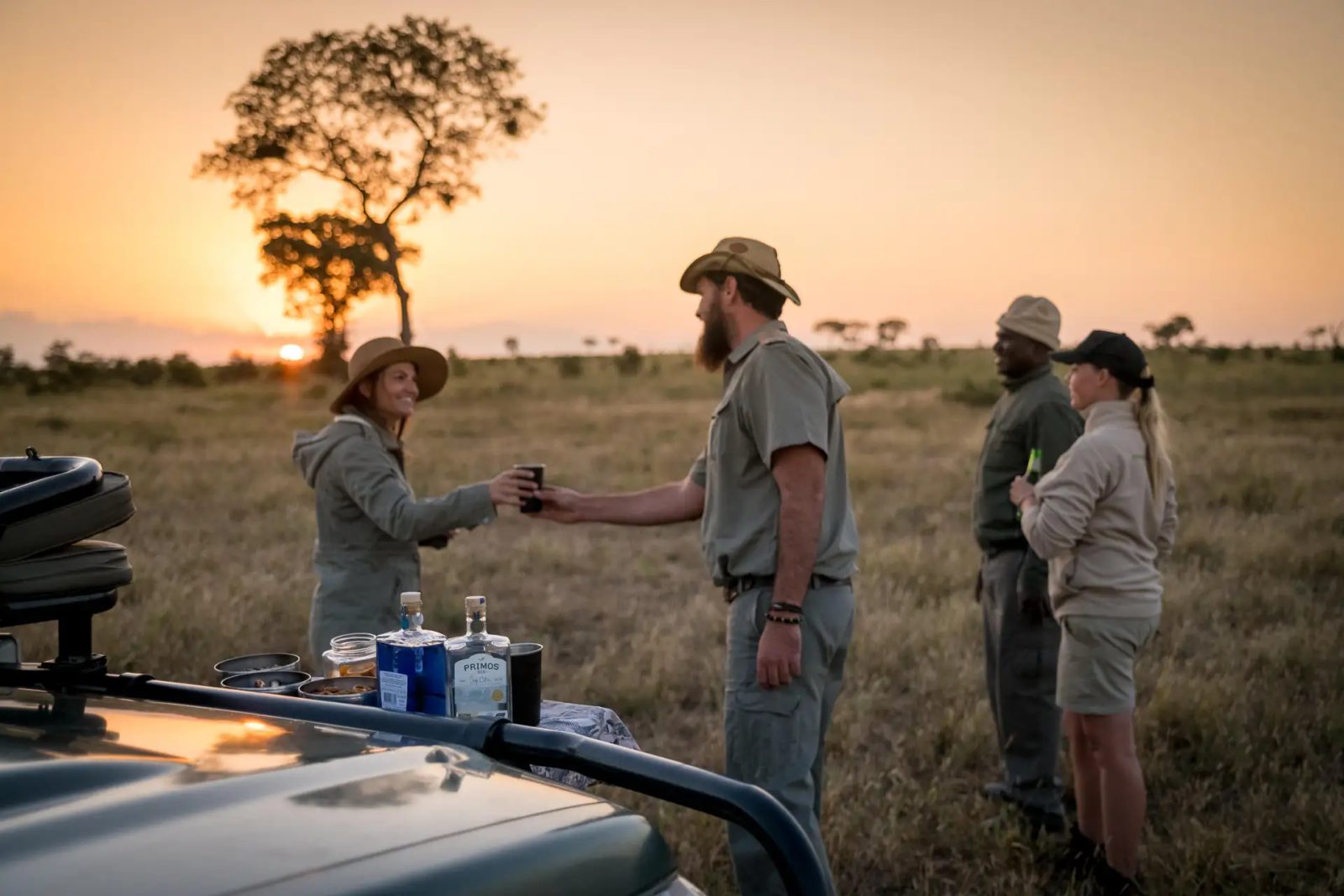 Guide handing a sundowner drink to a guest beside a game-drive vehicle at sunset, Umkumbe Safari Lodge