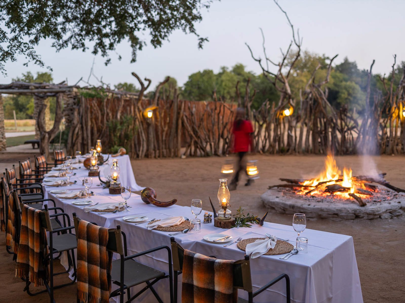 A long dinner table set beside a blazing boma fire at dusk at Karongwe