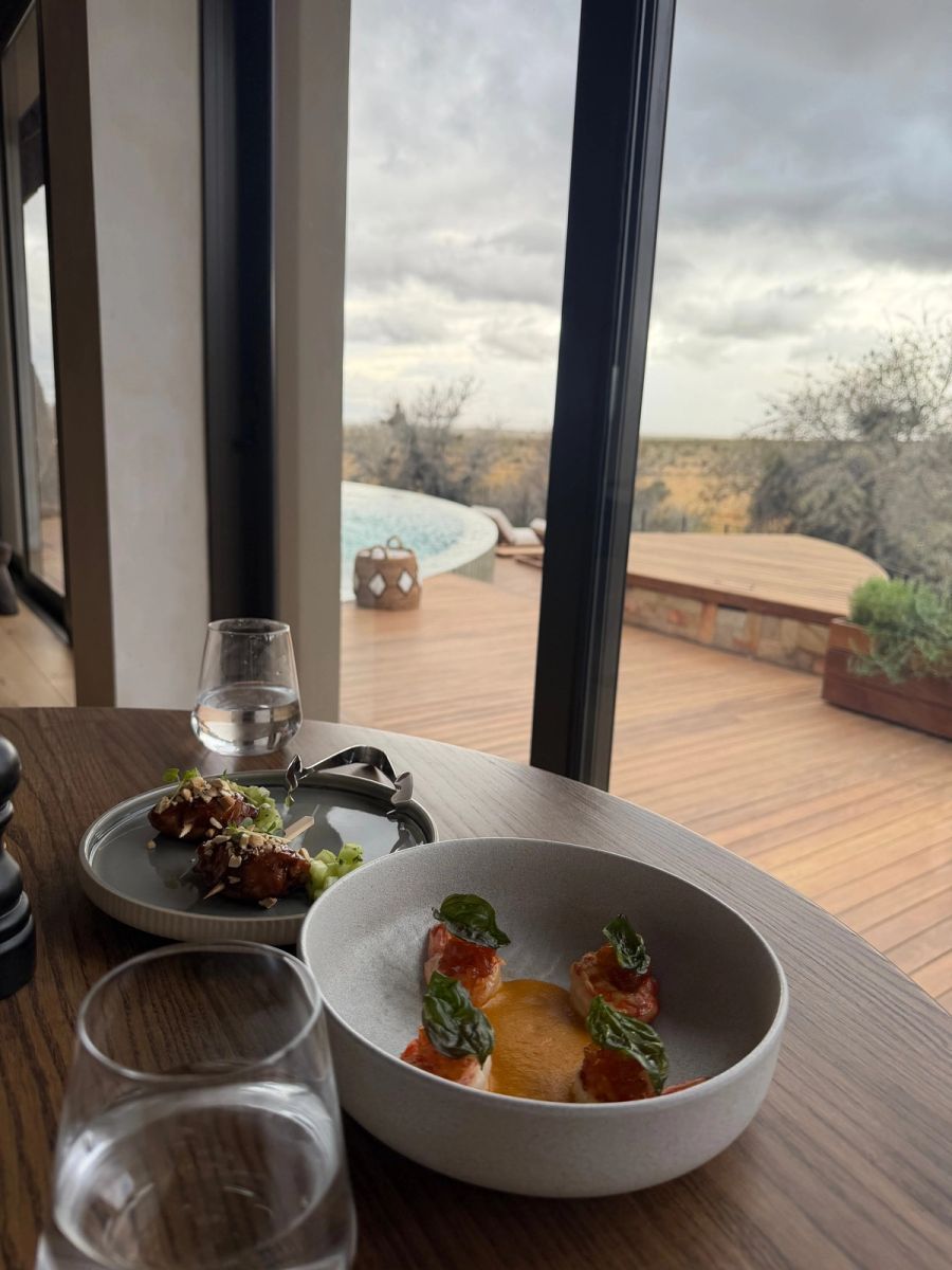 Chicken skewers and pan-fried prawns with fried basil on a table beside a window overlooking the deck and infinity pool at Kuganha