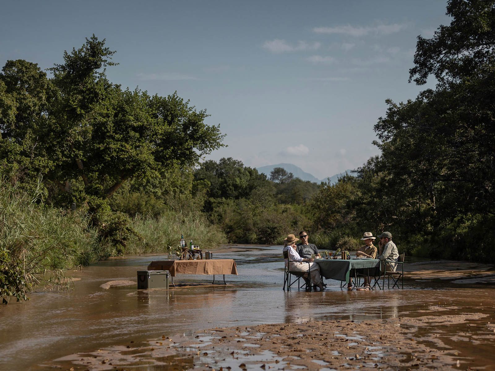 A breakfast table set in the shallows of a river at Karongwe, with mountains beyond