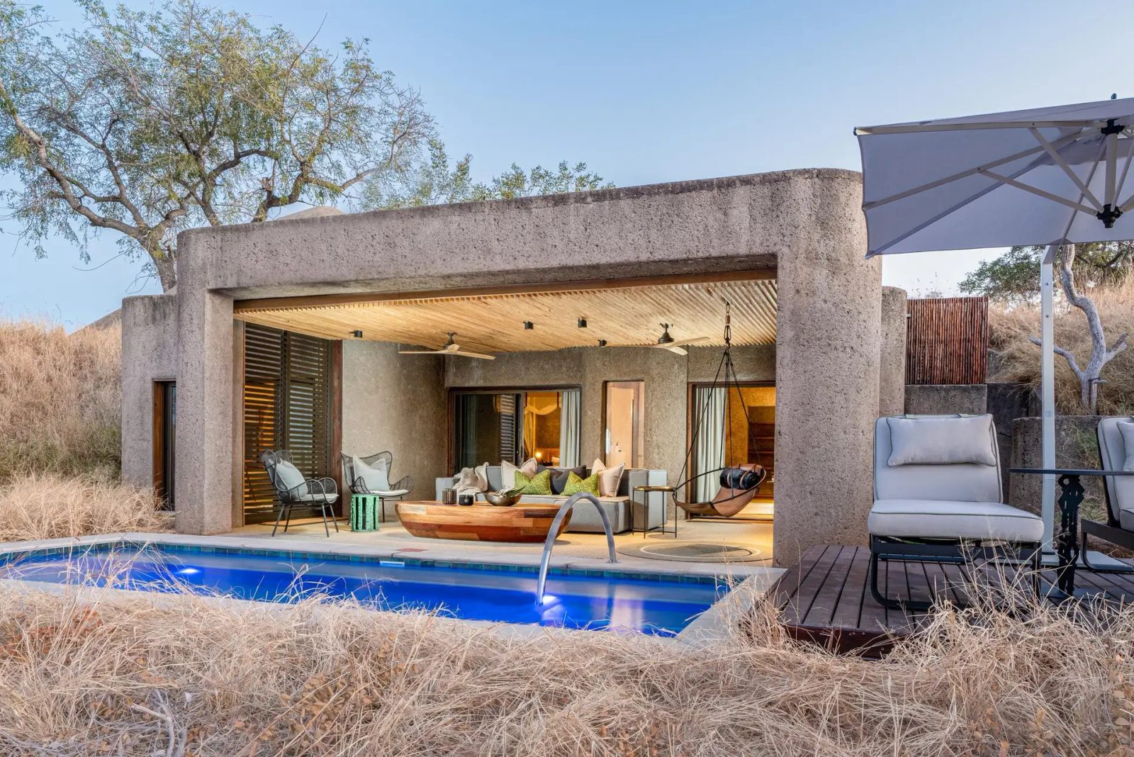 Sabi Sabi Earth Lodge suite exterior in raw concrete and timber with a private pool in dry golden grass