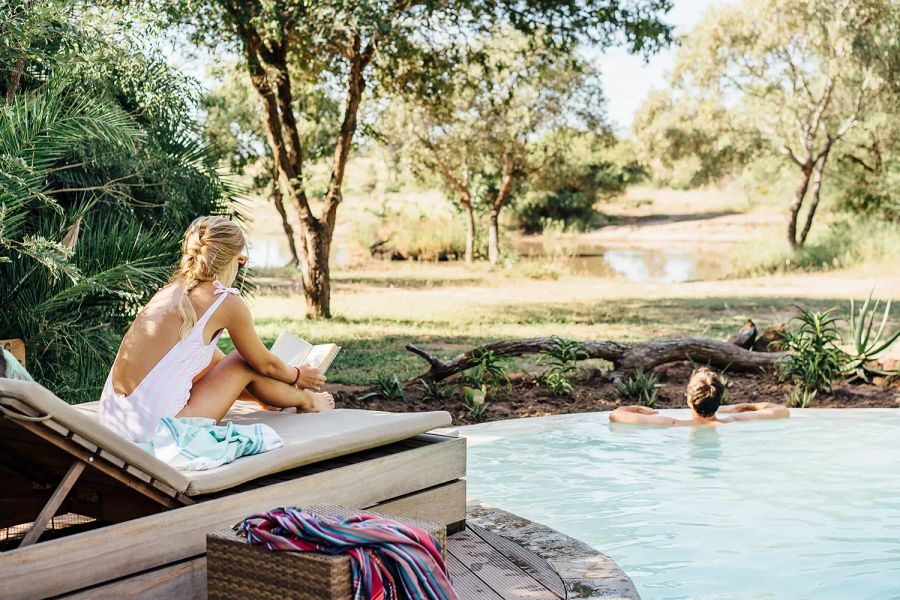Guests relaxing at the pool under trees at Tanda Tula Safari Camp, Timbavati