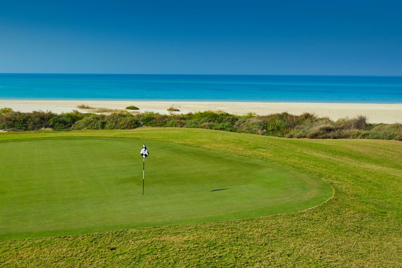 A coastal putting green at Saadiyat Beach Golf Course with the beach and Arabian Gulf beyond.
