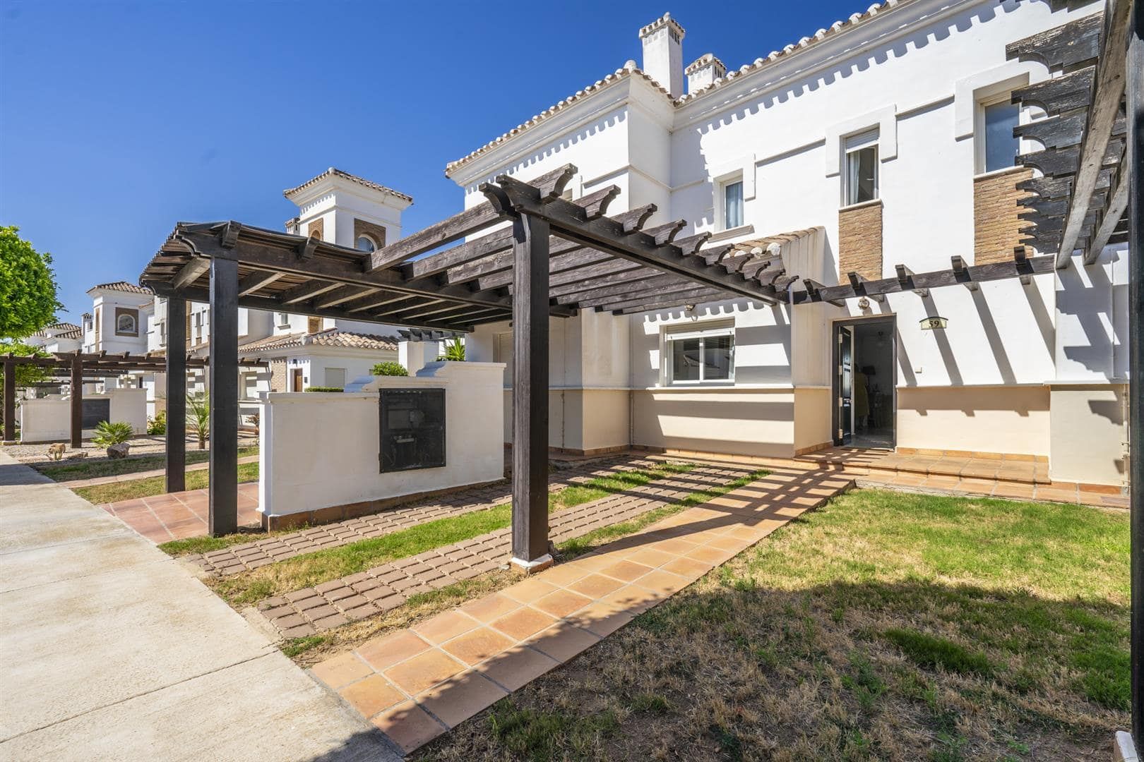 Front exterior of white resort townhouses with timber pergola parking.
