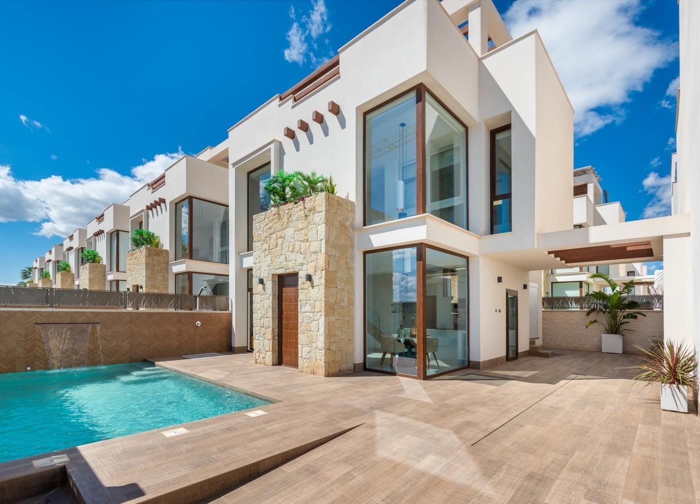Day exterior view of a white two-storey home with stone detailing, large glazing and a swimming pool