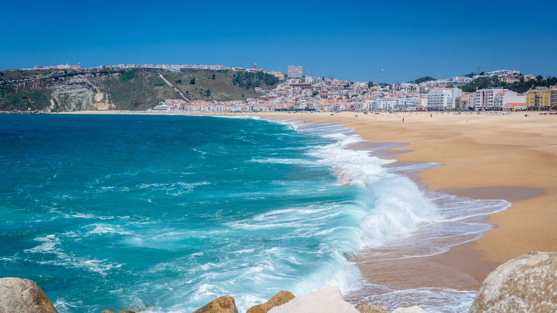 Atlantic waves breaking along a sandy beach, with a coastal town beyond