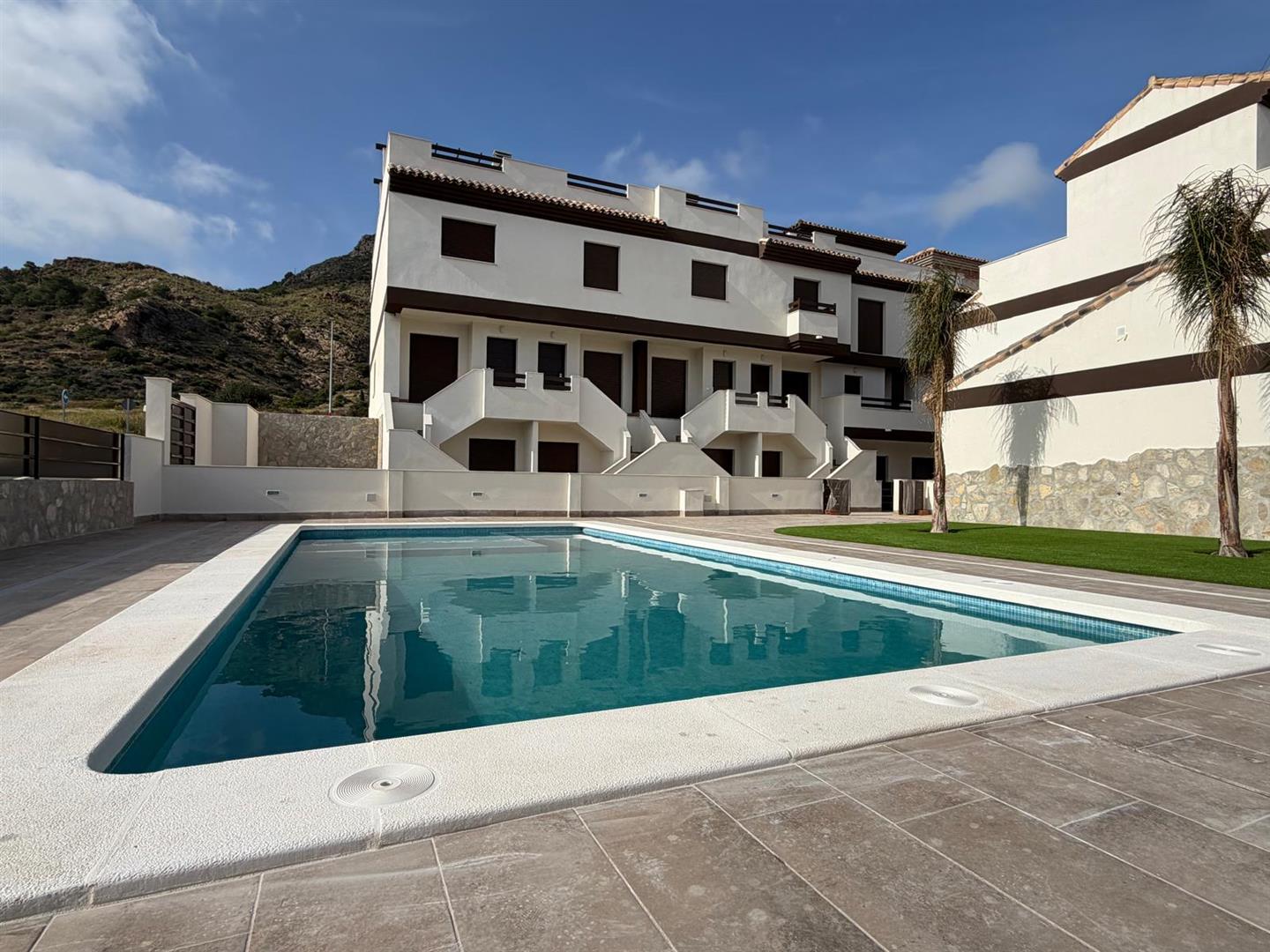 Communal swimming pool with the white townhouse terrace reflected in the water and hills behind