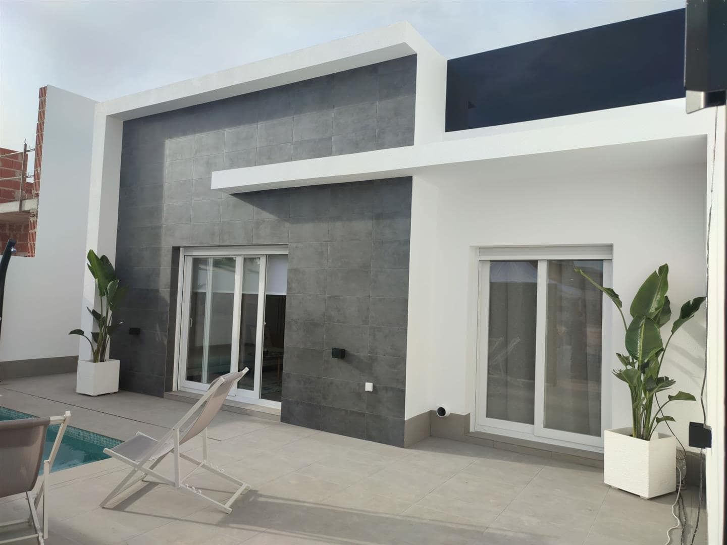Contemporary white and grey villa facade beside a tiled terrace and swimming pool edge