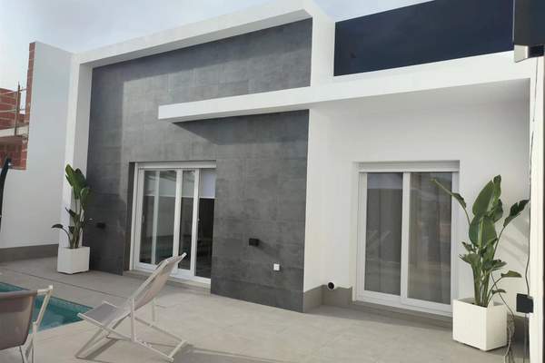 Contemporary white and grey villa facade beside a tiled terrace and swimming pool edge