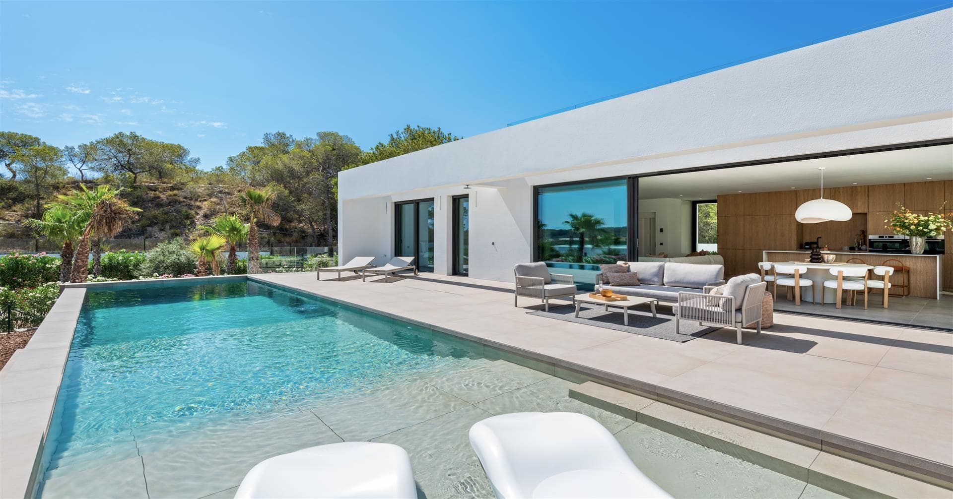 Photograph across a swimming pool towards a white villa with open living and dining terrace