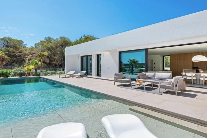 Photograph across a swimming pool towards a white villa with open living and dining terrace