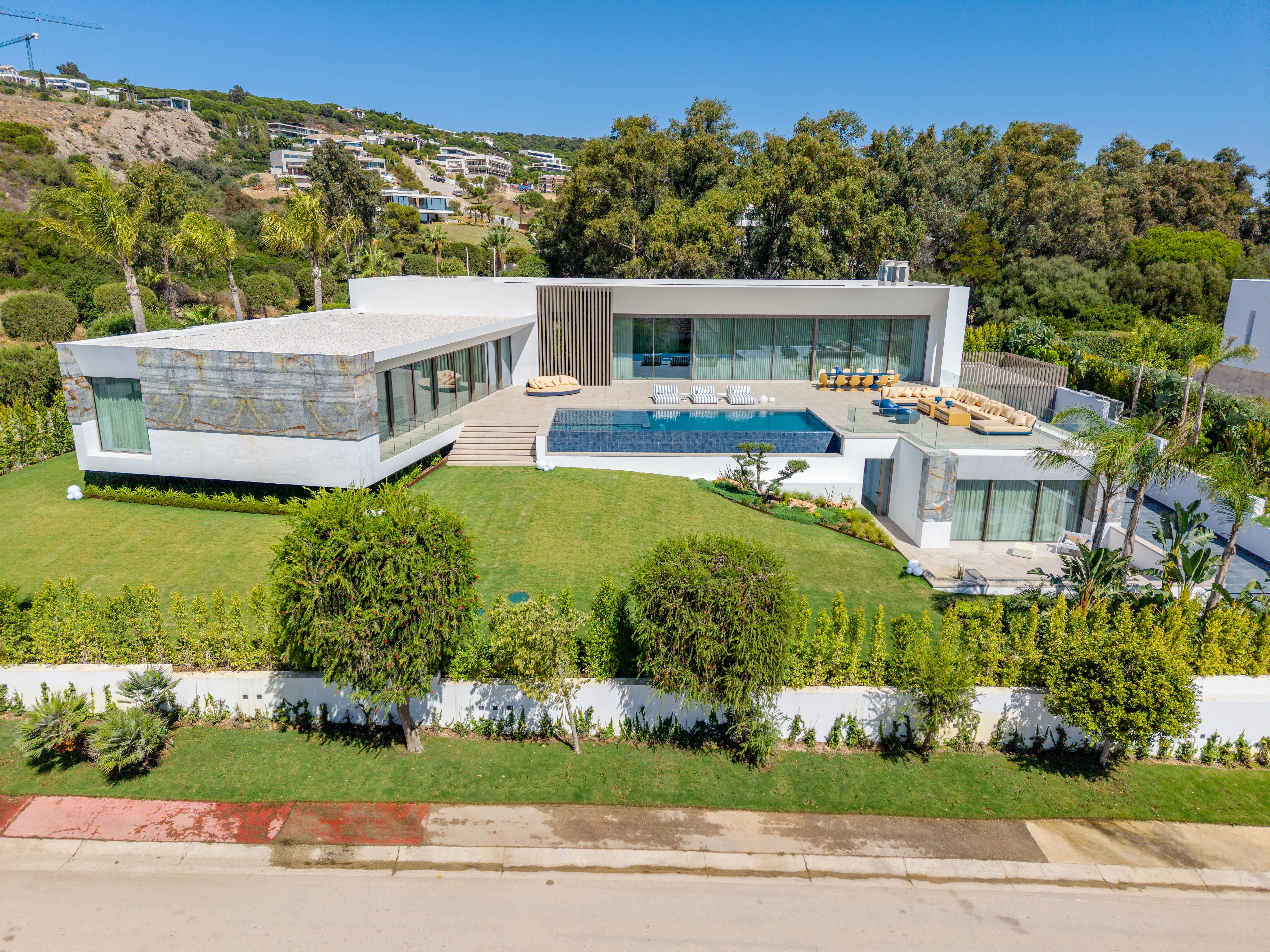 Aerial view of the contemporary villa with stone-clad wing, infinity pool terrace and lawned garden in La Reserva de Sotogrande