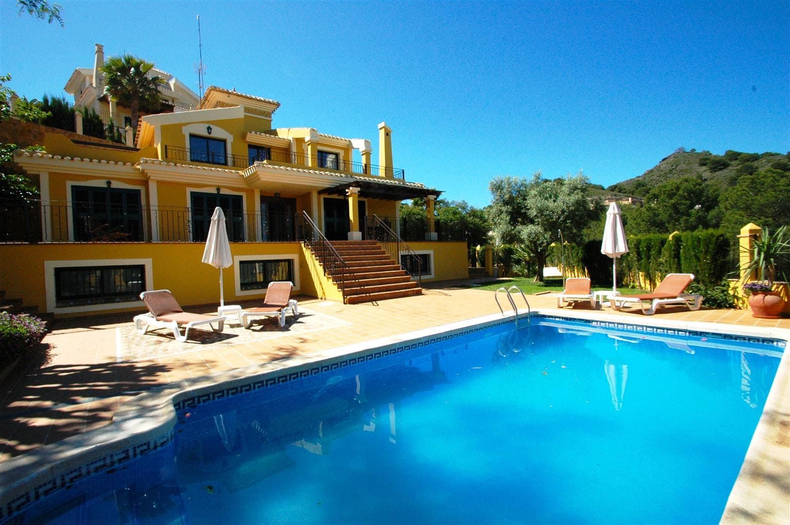 Yellow villa overlooking a large swimming pool and sun terrace.