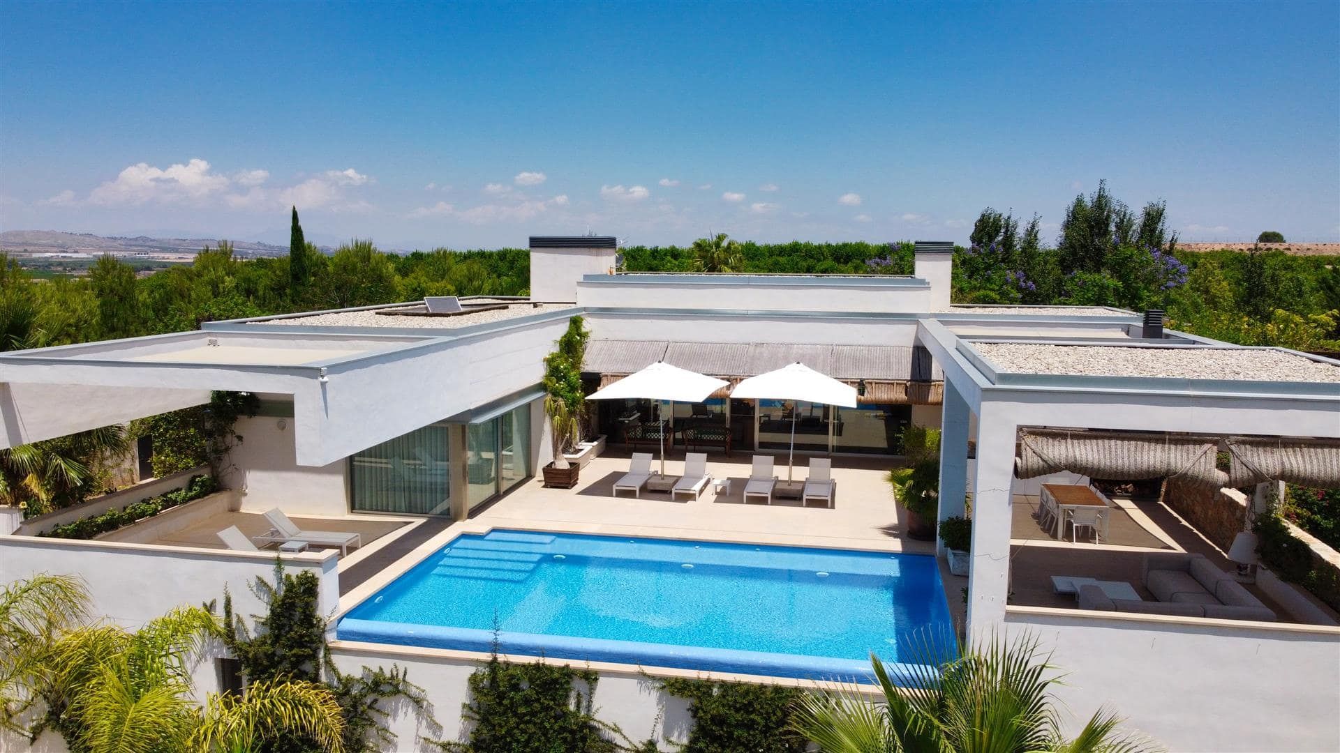Aerial view of the modern villa arranged around a blue swimming pool and terrace.