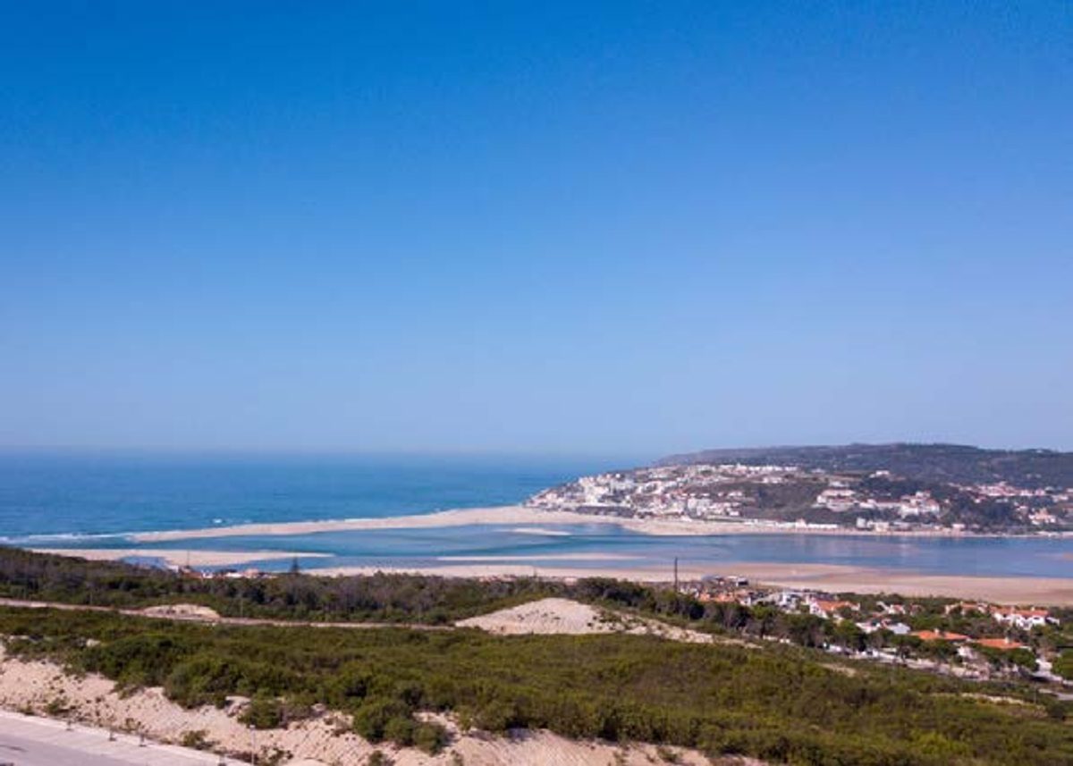 Sandbar between the calm Óbidos Lagoon and the Atlantic, with a hillside village above