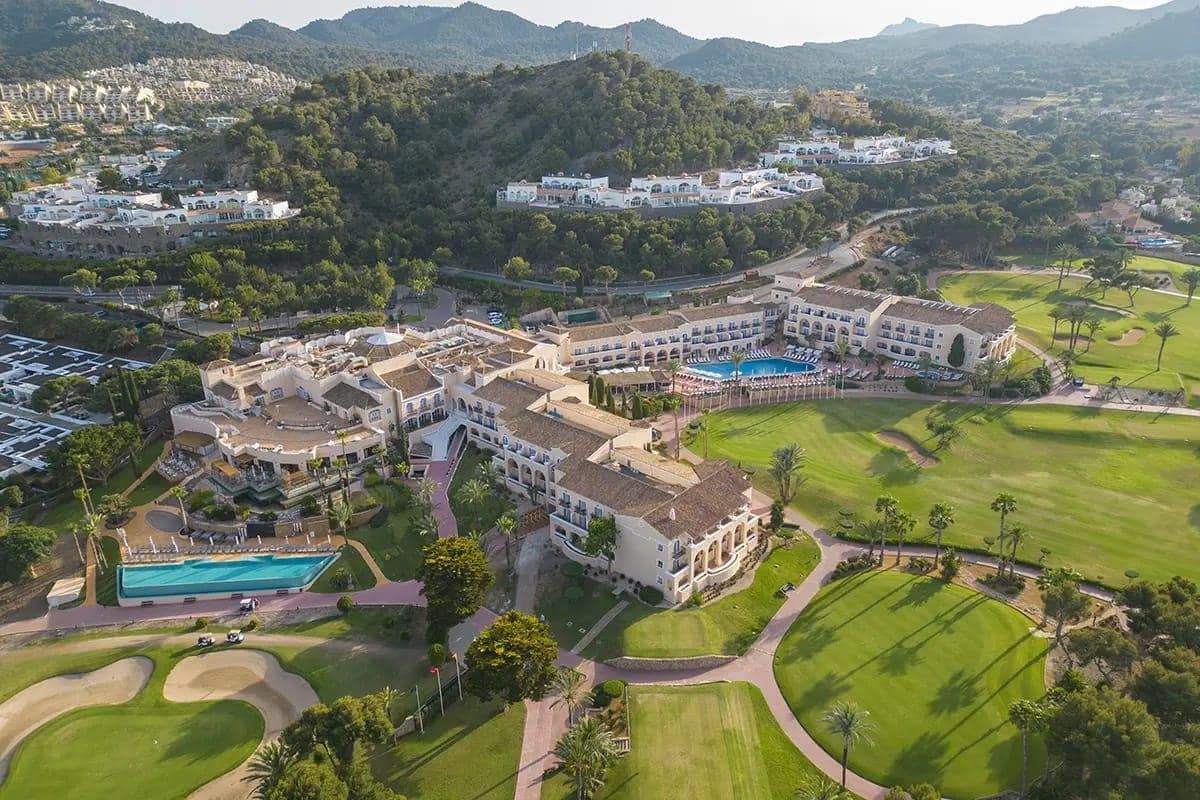 Aerial view of resort buildings, swimming pools and adjacent golf course.