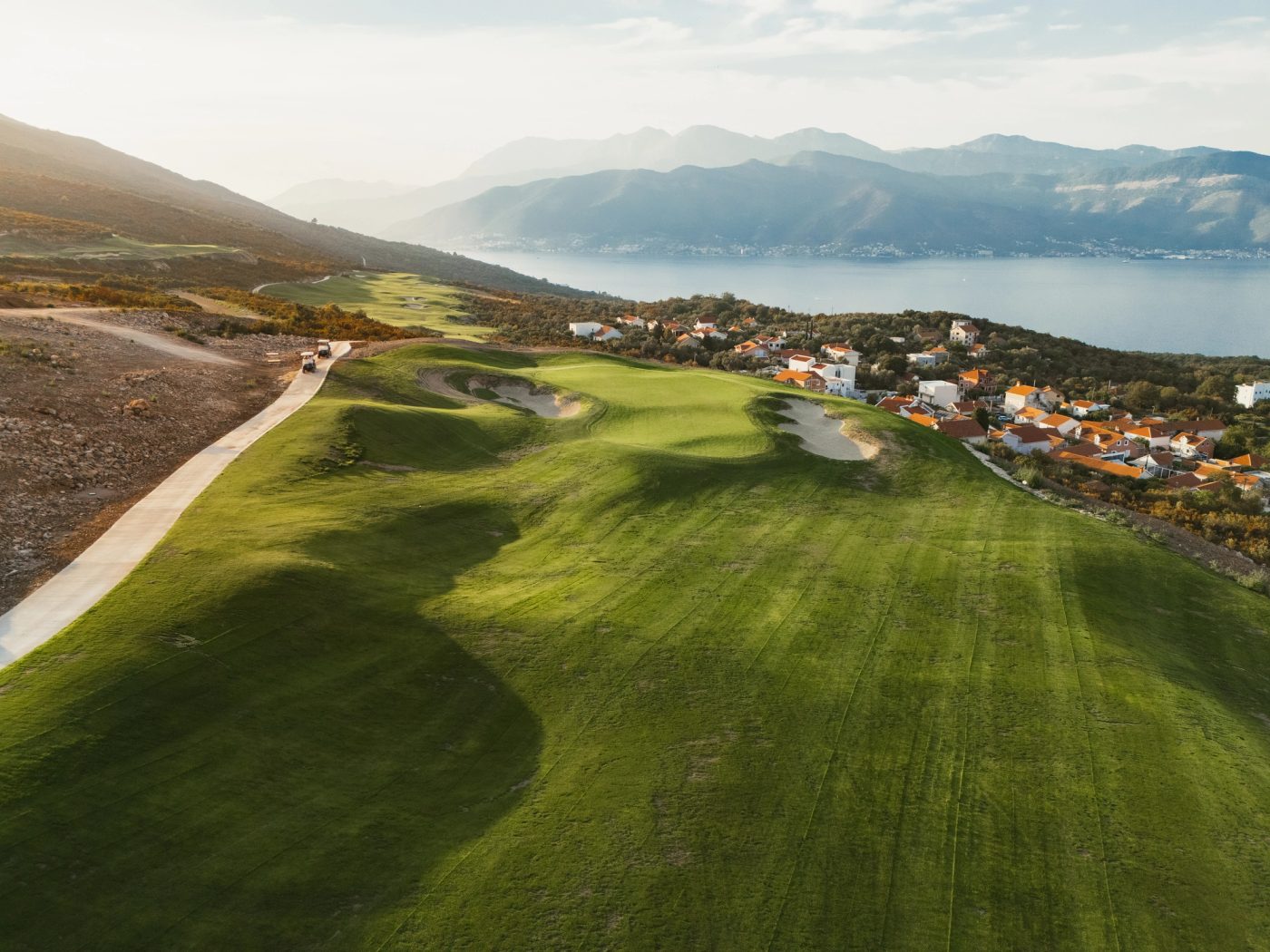 Aerial photograph of a golf green and bunkers at Luštica Bay, with the bay and mountains beyond