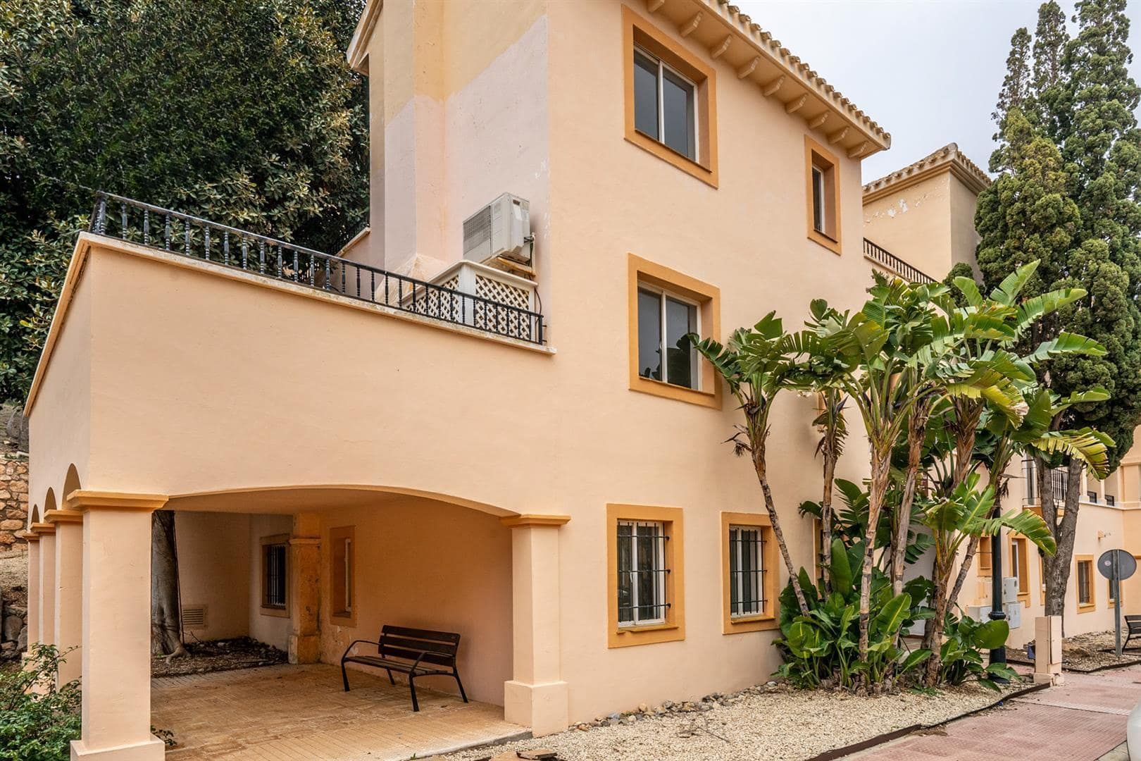 Peach-toned three-storey townhouse with an arched ground-floor entrance and mature planting.
