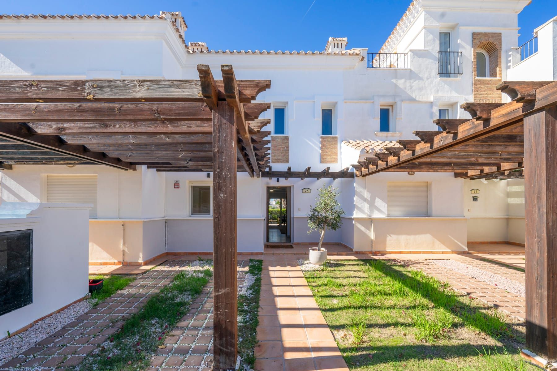 Front approach to white resort townhouses with timber pergola carports.