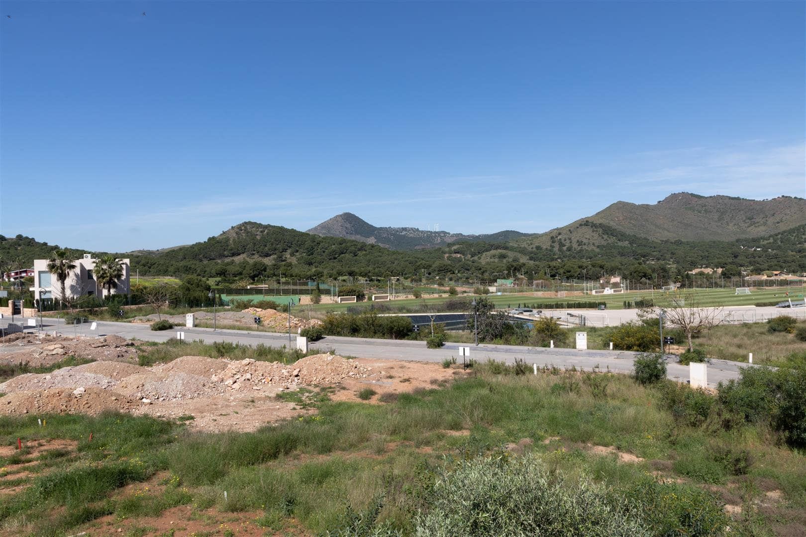 Photograph across undeveloped land and roads towards low hills beneath a clear sky