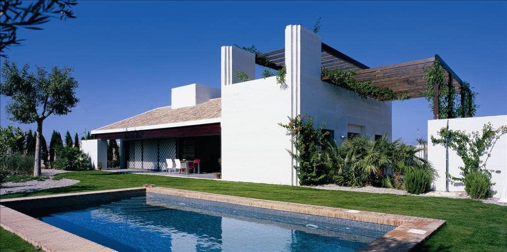 Wide exterior view of a white villa beside a swimming pool, lawn and planted garden
