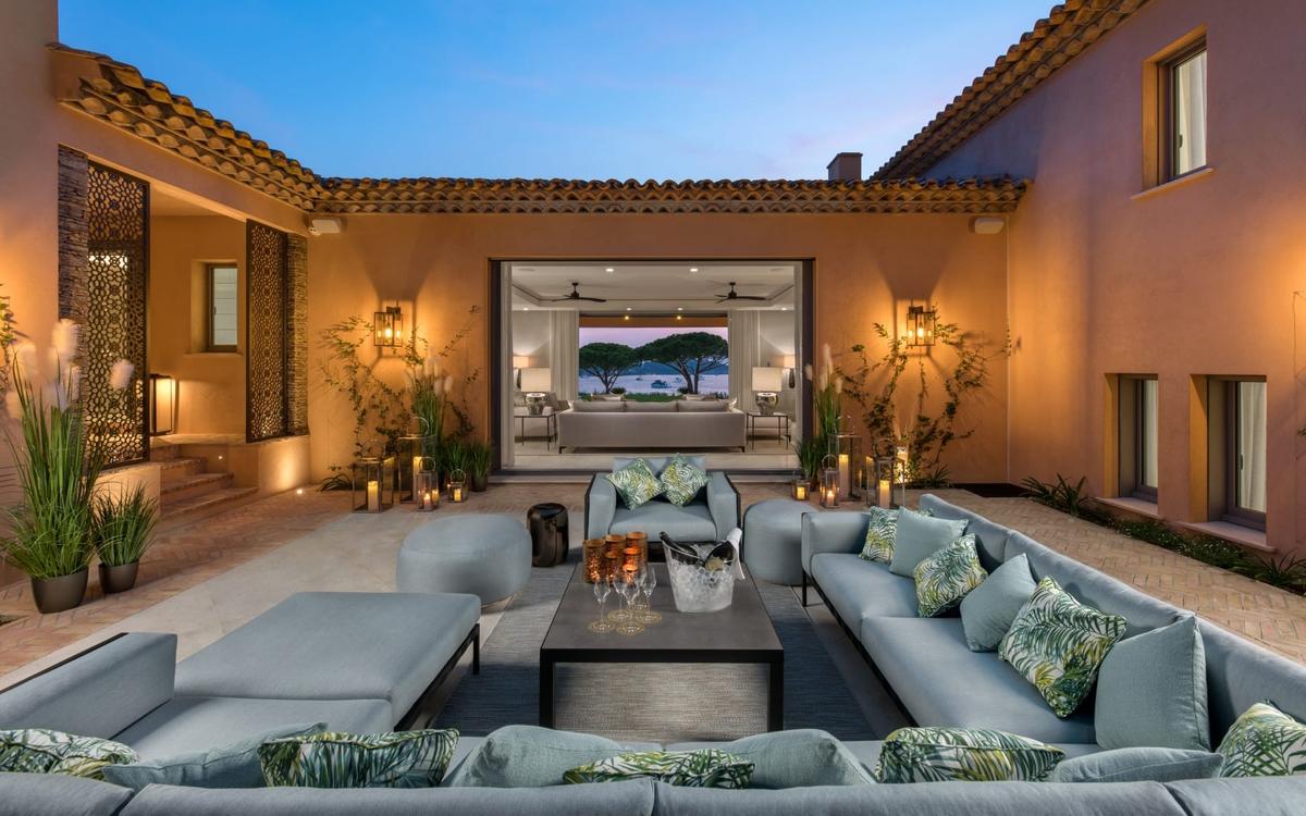 Warmly lit villa courtyard with outdoor seating and a sea view framed through the interior