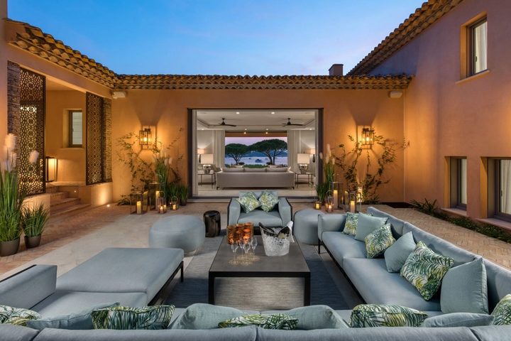 Warmly lit villa courtyard with outdoor seating and a sea view framed through the interior