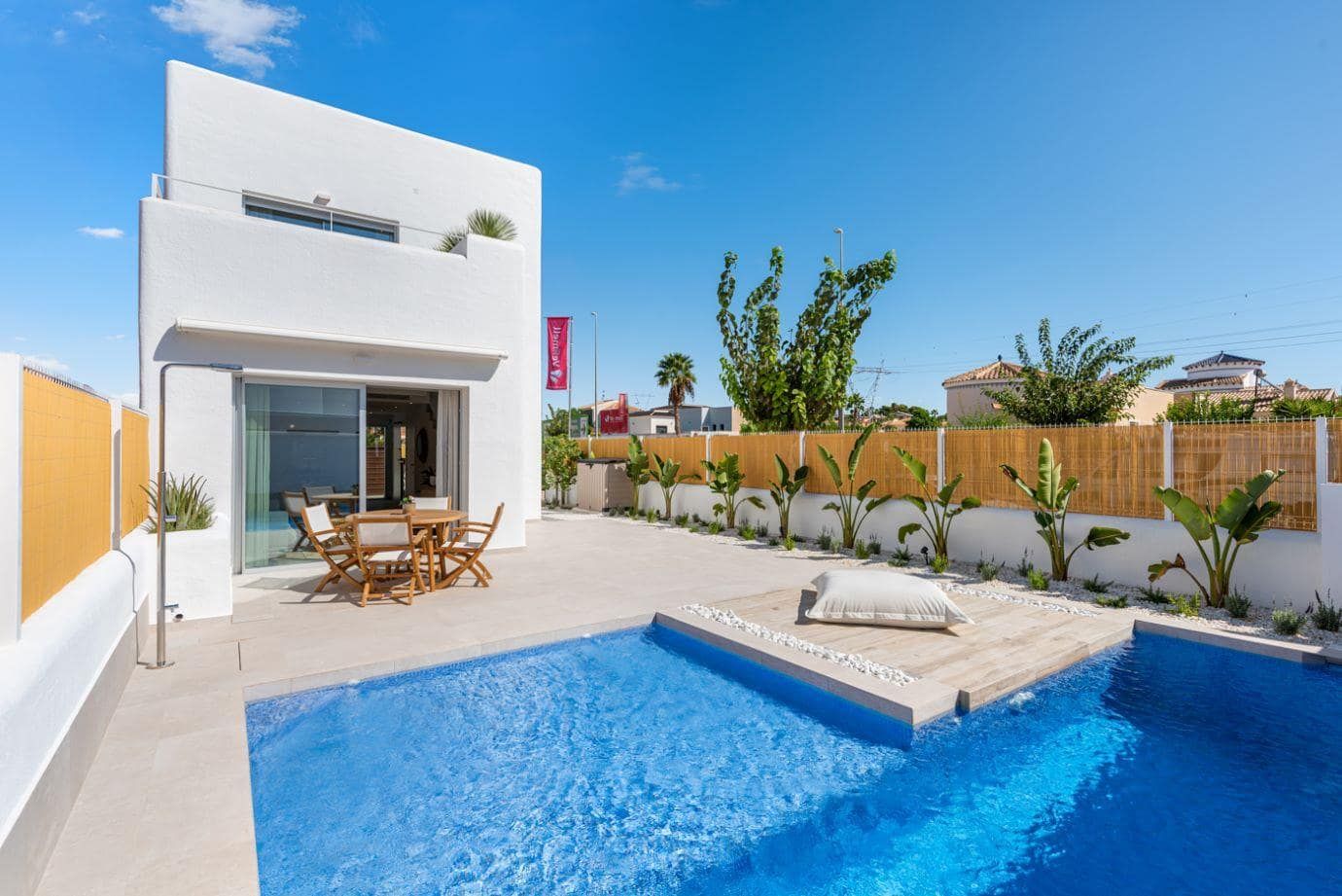 Photograph of a white villa beside a swimming pool and paved terrace in daylight