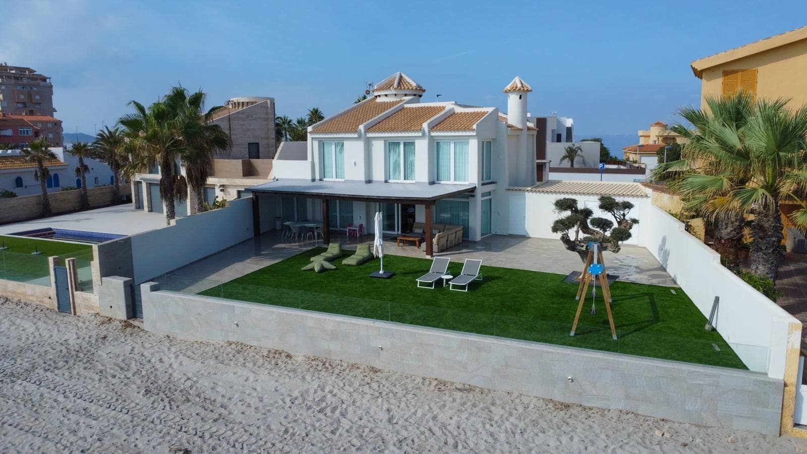 Beachfront villa facade with a broad lawn and sandy beach in the foreground.
