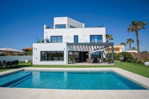 White canal-side villa with a swimming pool, lawn and shaded outdoor seating.