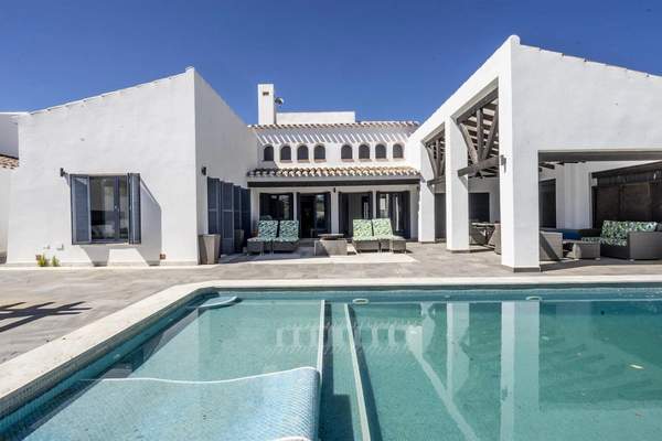 White villa arranged around a swimming pool and paved terrace under a clear blue sky.