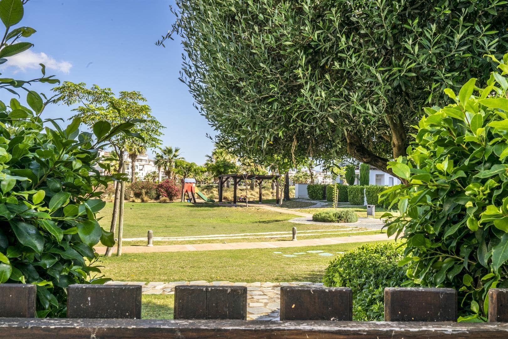 View through hedges towards landscaped communal gardens and a play area.