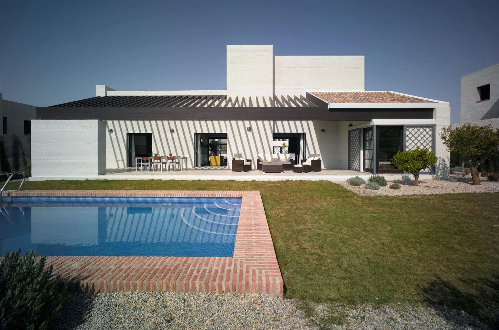 Rear exterior of a white villa with garden terrace and swimming pool in daylight