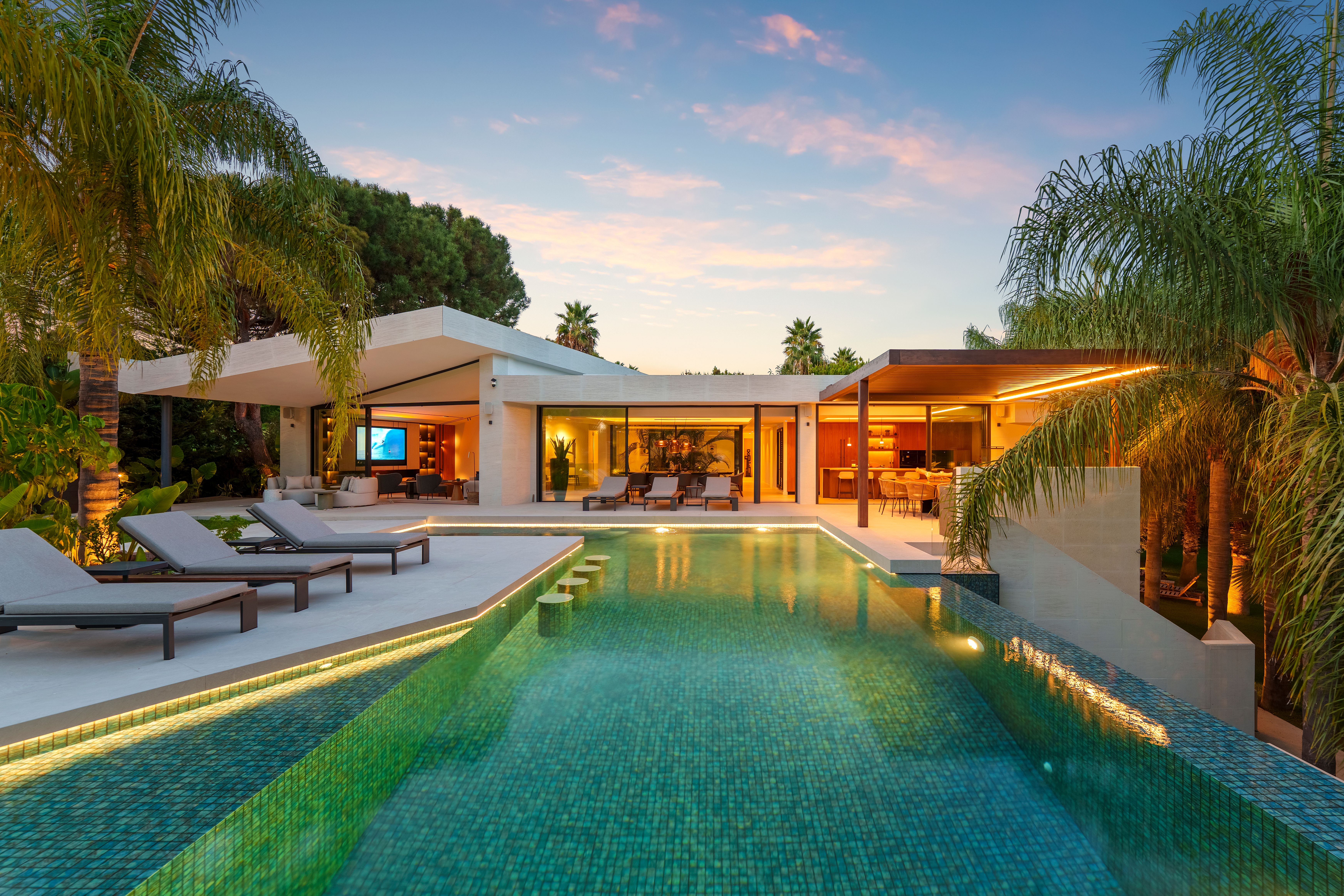 Blue-hour pool view with the villa and terraces warmly illuminated