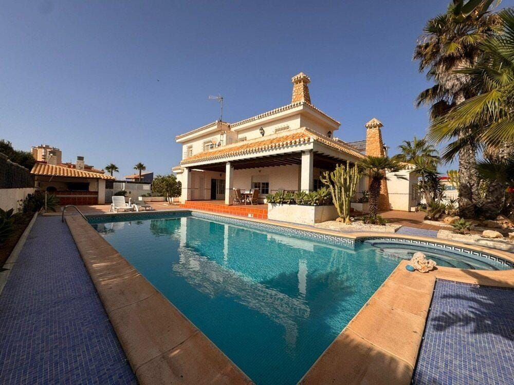 Large villa facade and covered terrace reflected in a blue swimming pool.