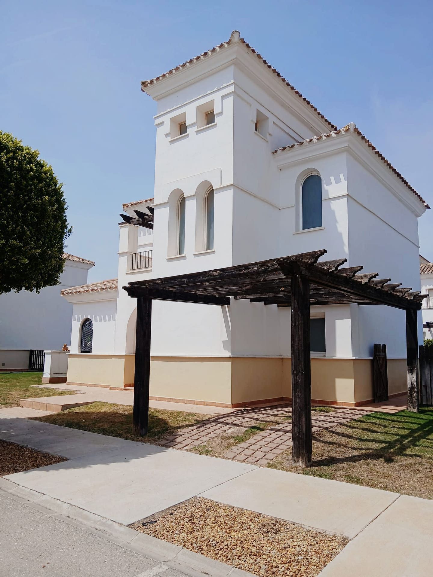 Day exterior view of a white multi-level home with arched windows and a timber pergola